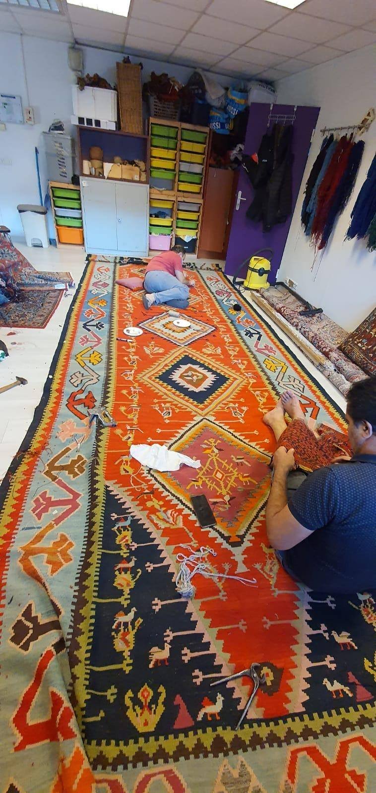 Un kilim de plusieurs mètres repris à deux, à même le sol de l’atelier.